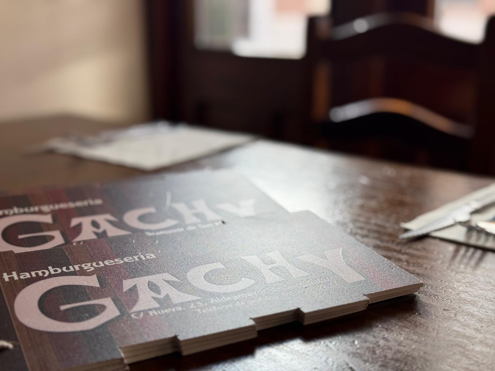 Cartas del menú de Hamburguesería Gachy sobre mesa de madera.